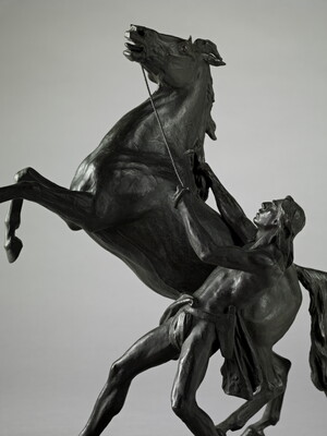 A bronze sculpture of a Native American man holding back a rearing horse.