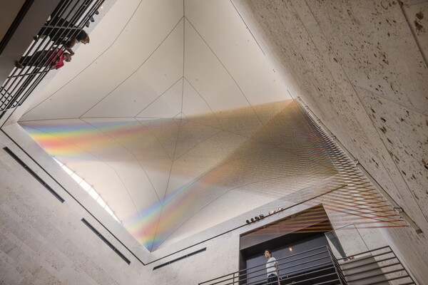 A large installation of multicolored sewing thread that stretches from one wall to the ceiling in the Carter's Atrium and looks like a rainbow.