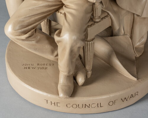 A detail of a sculpture of Abraham Lincoln, seated, reading a paper between two standing men.