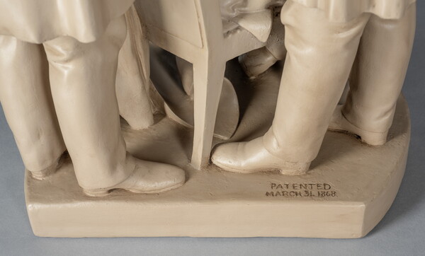 A detail of a sculpture of Abraham Lincoln, seated, reading a paper between two standing men.