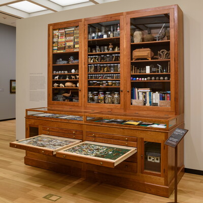 A large wooden cabinet with drawers on the bottom half and glass-fronted cabinets above, all filled with random objects.