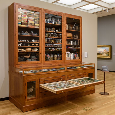 A large wooden cabinet with drawers on the bottom half and glass-fronted cabinets above, all filled with random objects.