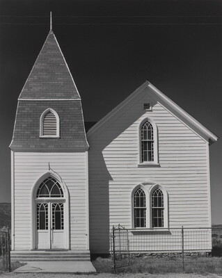 A black-and-white photograph of a two-story church with white clapboard siding and arched windows and doors.