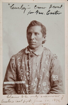 A sepia-toned portrait of an Indigenous man wearing a hide jacket with decorative stitching.