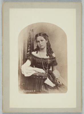A sepia-toned portrait of a light-skinned teenage girl, seated in a chair, wearing a formal, off-the-shoulder dress with her hair styled in ringlets that fall over her shoulder.