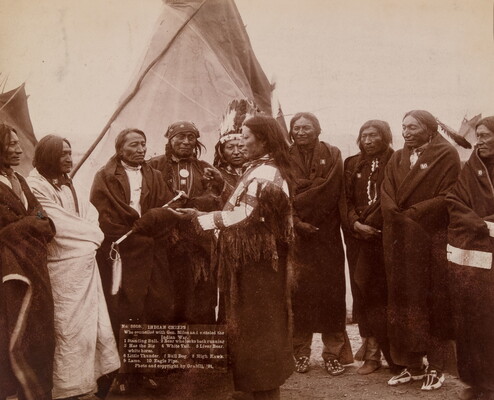 A sepia-toned photograph of Indigenous men wrapped in blankets meeting in front of a tipi.