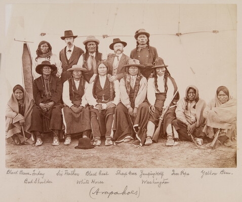 A sepia-toned photograph of a group of Indigenous people, some standing and some sitting.