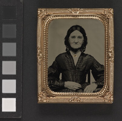 A black-and-white photograph in a decorative gold frame of an elderly White woman in spectacles wearing a dark Victorian-style dress.