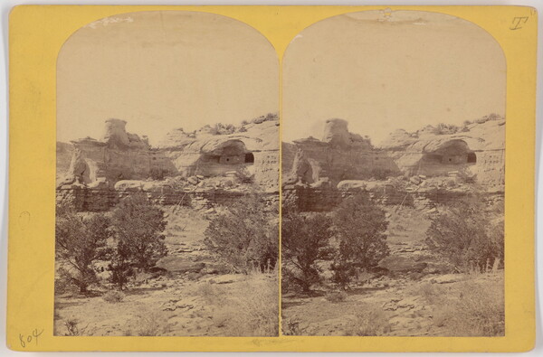 Two almost identical side-by-side sepia-toned photographs of cave dwellings in a high cliff with scrubby vegetation in the foreground.