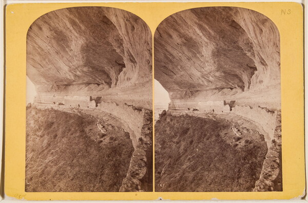 Two almost identical side-by-side sepia-toned photographs of a ruined stone structure built under the overhang of a cliff.