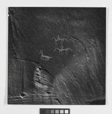 A black-and-white photograph of rock paintings depicting people on horseback and a deer.