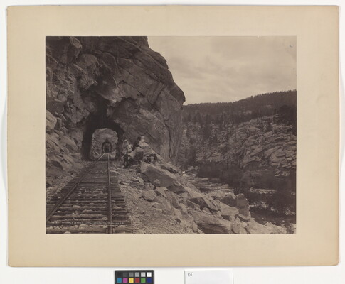 A black-and-white photograph of a train track stretching through a series of rock tunnels in the side of a mountain.