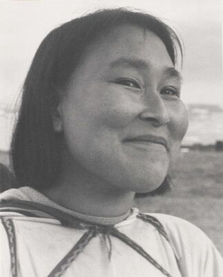 A black-and-white photograph of a close-up of a smiling Indigenous woman with short dark hair wearing a light-colored shirt.