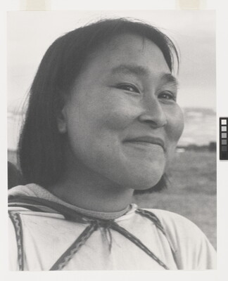 A black-and-white photograph of a close-up of a smiling Indigenous woman with short dark hair wearing a light-colored shirt.