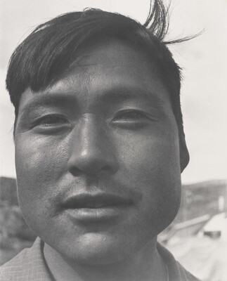 A black-and-white photograph of a close-up of an Indigenous man with short dark hair, one lock sticking up at back.