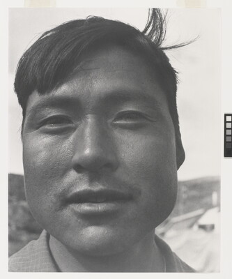 A black-and-white photograph of a close-up of an Indigenous man with short dark hair, one lock sticking up at back.