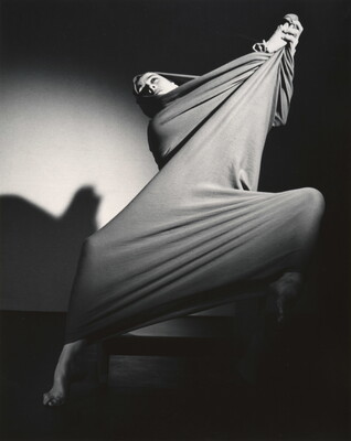 A black-and-white photograph of a modern dancer wrapped in a piece of cloth that she is stretching into shapes over her body.