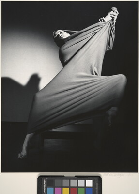 A black-and-white photograph of a modern dancer wrapped in a piece of cloth that she is stretching into shapes over her body.