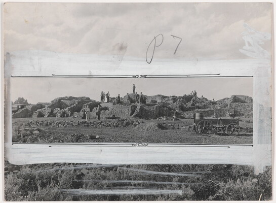 A black-and-white photograph of people standing on an excavation site; crop marks and white paint mark how the photo should be cropped.