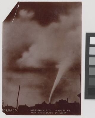 A sepia-toned photograph of a white funnel cloud above the silhouette of a town.