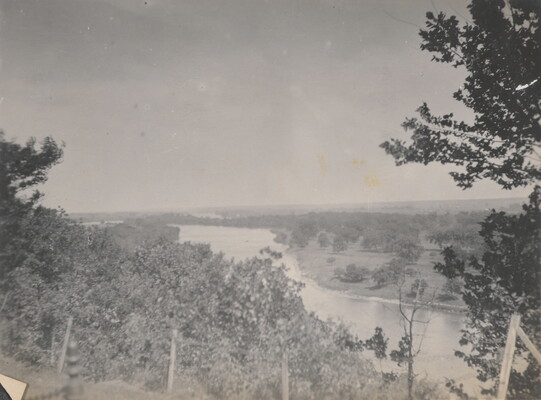 A black-and-white photograph taken from a higher elevation of a river and surrounding fields and trees.