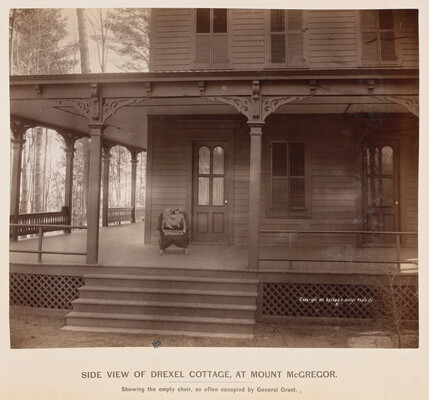 A black-and-white photograph of a two-story clapboard house with steps leading up to a chair on a wrap-around porch.