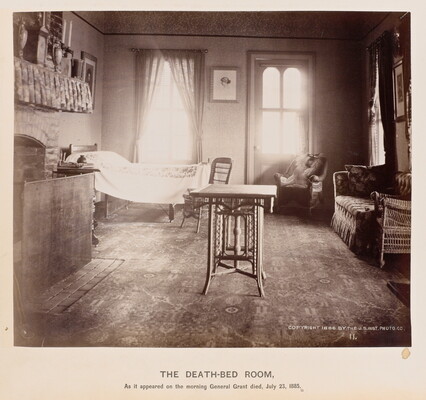 A black-and-white photograph of a sun-drenched bedroom interior with a bed, a chair, and a sofa along the wall, and a small table in the center of the room.