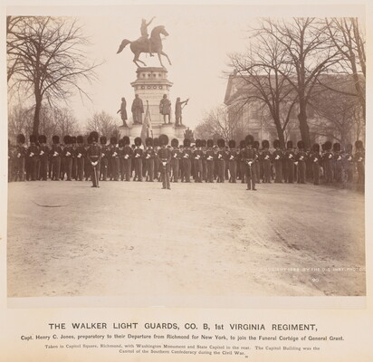 A sepia-toned photograph of a group of men in military outfits standing shoulder to shoulder in front of a monument of a man on horseback.