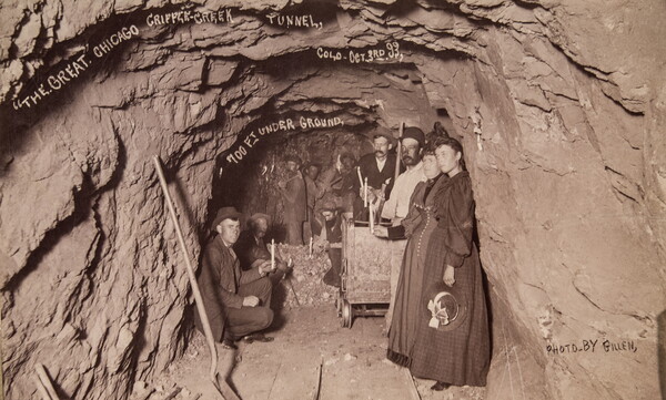 A sepia-toned photograph of a group of people in an underground rock tunnel.