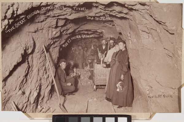 A sepia-toned photograph of a group of people in an underground rock tunnel.