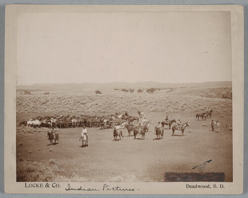 A black-and-white photograph of a large group of cowboys on horseback lined up in an open field.