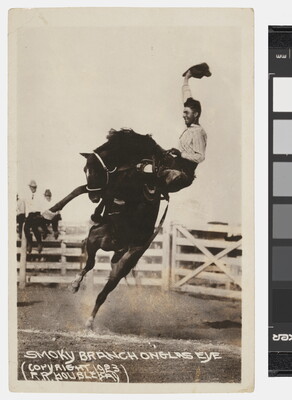 A black-and-white photograph of a cowboy waving his hat as he holds on to a rearing horse at an outdoor rodeo.