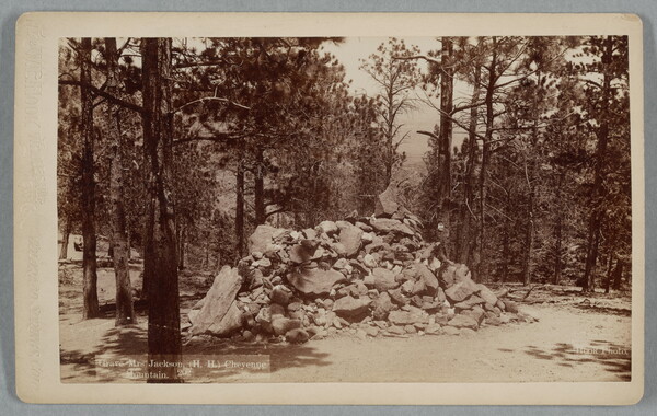 A black-and-white photograph of a large pile of rocks in a wooded area.
