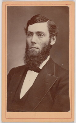 A black-and-white portrait photograph of the head and shoulders of a formally dressed White man with a full beard.
