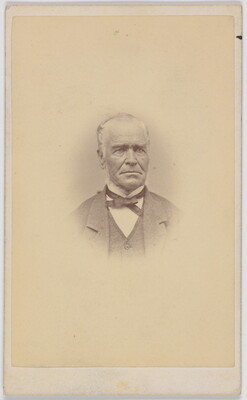 A black-and-white portrait photograph of an older White man, balding, wearing a bow tie, jacket, and vest.