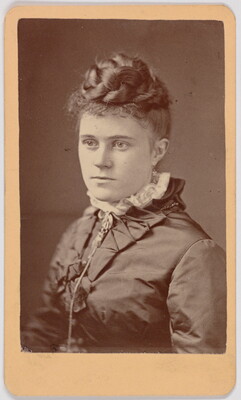 A black-and-white portrait photograph of a young White woman, hair braided and piled on top of her head, wearing a dark dress with a high lace collar.