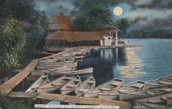 A color postcard photograph of a row of rowboats lined up along a dock leading to a boathouse; moonlight reflecting on the water.