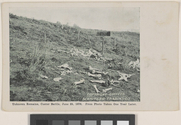 A black-and-white photograph of a field with human bones scattered everywhere and a wooden sign that reads, "UNKNOWN."