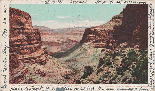 A color postcard of red rocks and a green valley of a canyon with black cursive handwriting around the border.