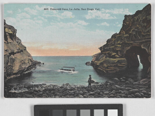 A color postcard of a person on a rocky shoreline watching a boat on the water.