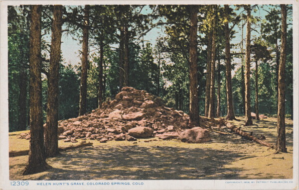 A colored photograph on a postcard of a large pile of rocks and boulders surrounded by tall pine trees.