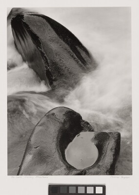 A black-and-white photograph of steam rising from two rocks, one with a pool of water in it.