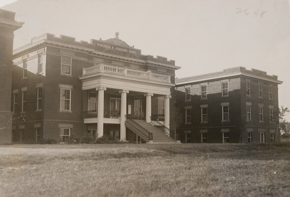 A black-and-white photograph of a three-story building with a large staircase that leads to a columned entrance.