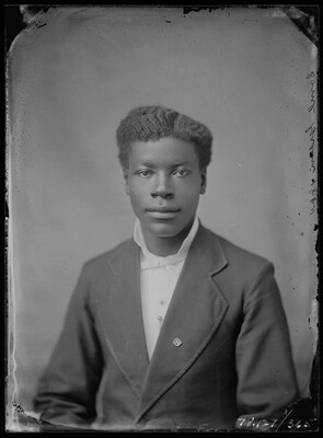 A black-and-white studio image of a young Black man wearing a suit jacket over a white shirt.