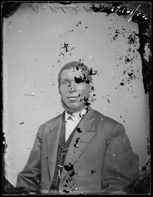 A black-and-white portrait image of a Black man wearing a suit and vest; the image has some black splotches and scratches on the surface.