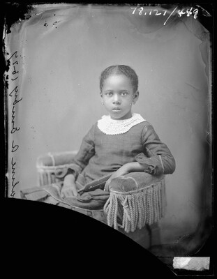 A black-and-white studio image of a seated Black girl wearing a dress with a lace collar.