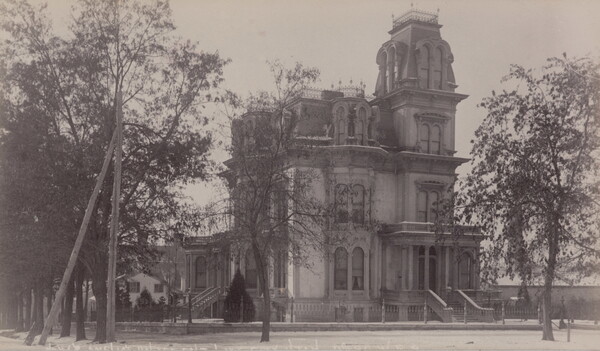 A black-and-white photograph of a four-story Victorian-style mansion with arched windows and a tower.