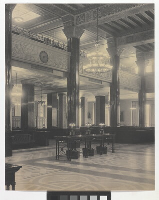 A black-and-white photograph of the interior of an ornate office lobby with inlaid floors, columns, and chandeliers.