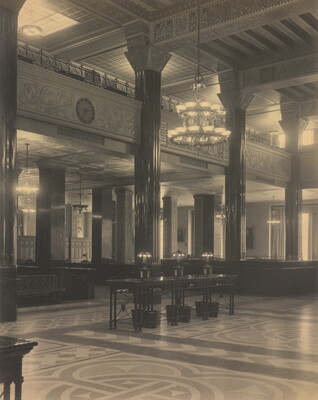 A black-and-white photograph of the interior of an ornate office lobby with inlaid floors, columns, and chandeliers.