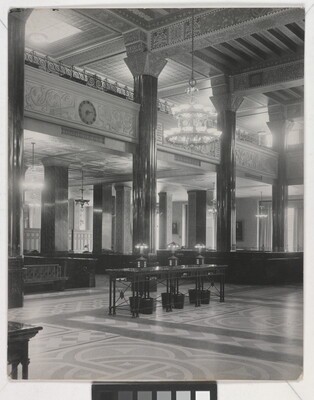 A black-and-white photograph of the interior of an ornate office lobby with inlaid floors, columns, and chandeliers.